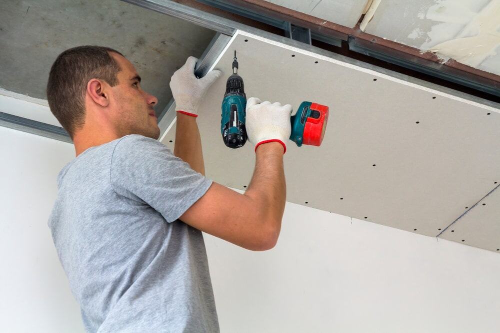 Skilled professional installing ceiling panels with power drill in home renovation.