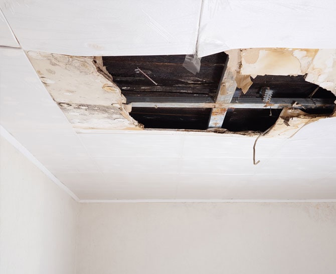 Close-up of damaged ceiling with holes and exposed wiring in a residential space.
